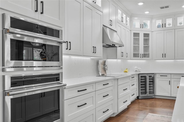 kitchen featuring double oven, black electric cooktop, under cabinet range hood, beverage cooler, and light countertops