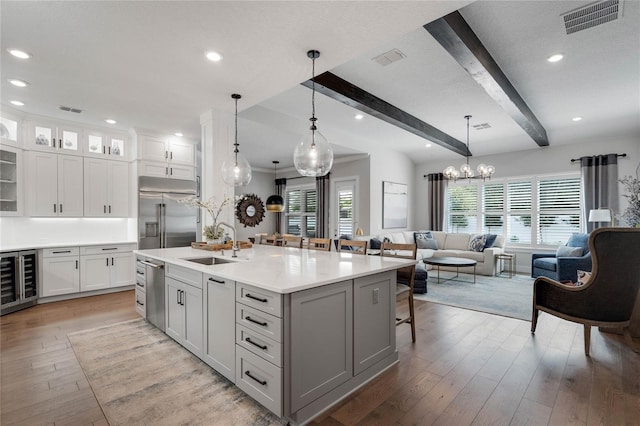 kitchen featuring visible vents, wine cooler, appliances with stainless steel finishes, beamed ceiling, and a sink