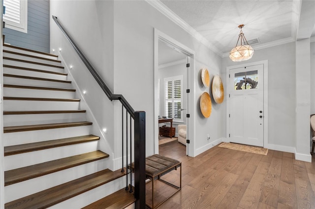 entrance foyer featuring hardwood / wood-style flooring, visible vents, baseboards, stairs, and ornamental molding