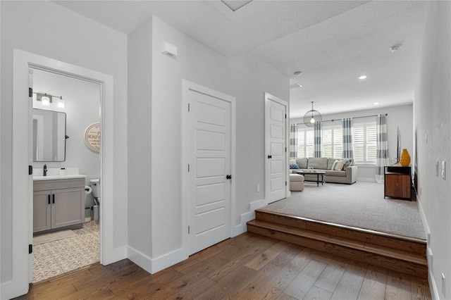 hall featuring a textured ceiling, hardwood / wood-style floors, a sink, and baseboards