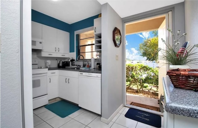 kitchen featuring white appliances, dark countertops, white cabinetry, a sink, and light tile patterned flooring