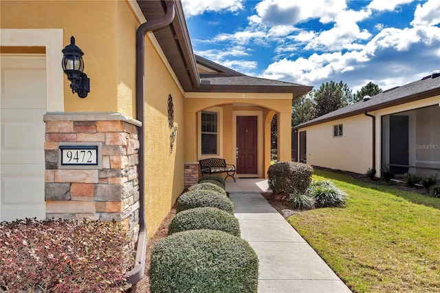 entrance to property with stone siding, a yard, and stucco siding