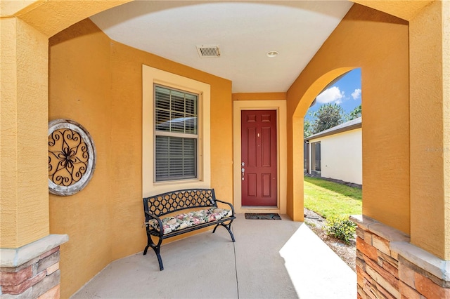 entrance to property featuring a porch, visible vents, and stucco siding