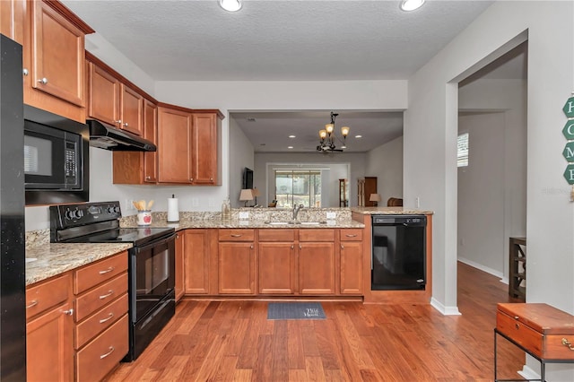 kitchen featuring brown cabinets, a sink, wood finished floors, under cabinet range hood, and black appliances