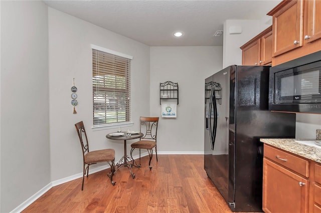 kitchen with brown cabinetry, baseboards, light wood finished floors, and black appliances