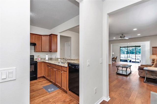 kitchen with black appliances, light wood-style flooring, light stone counters, and a sink