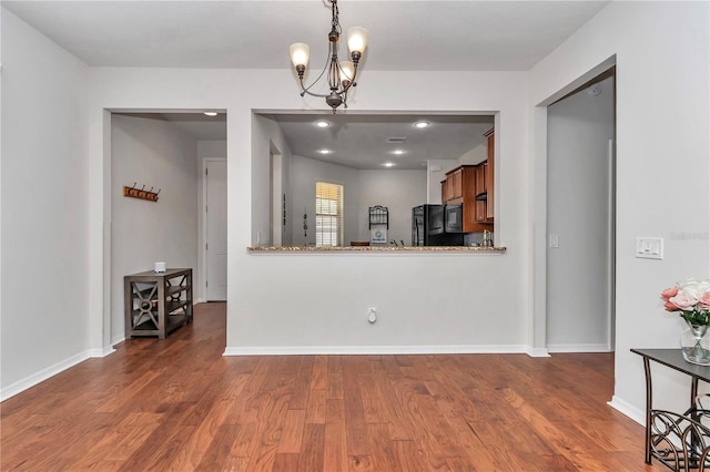 kitchen featuring baseboards, brown cabinetry, wood finished floors, black appliances, and a chandelier