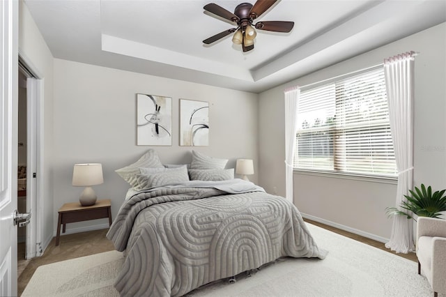 bedroom featuring baseboards, a tray ceiling, and ceiling fan