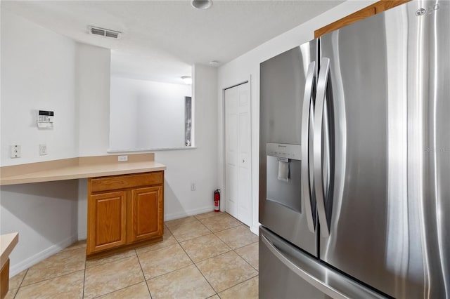 kitchen featuring built in desk, stainless steel refrigerator with ice dispenser, visible vents, light countertops, and brown cabinetry