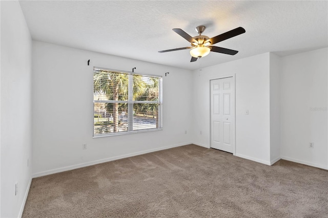 empty room featuring ceiling fan, a textured ceiling, baseboards, and carpet flooring