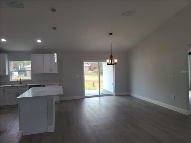 kitchen featuring a center island, light countertops, hanging light fixtures, white cabinetry, and a sink