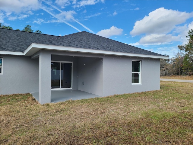 rear view of house featuring a patio area, roof with shingles, a lawn, and stucco siding