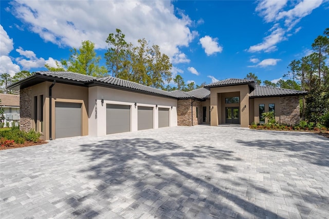 prairie-style home with a garage, decorative driveway, stone siding, and stucco siding