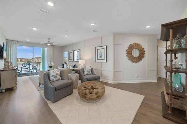 living room featuring a textured ceiling, a decorative wall, wood finished floors, a ceiling fan, and visible vents