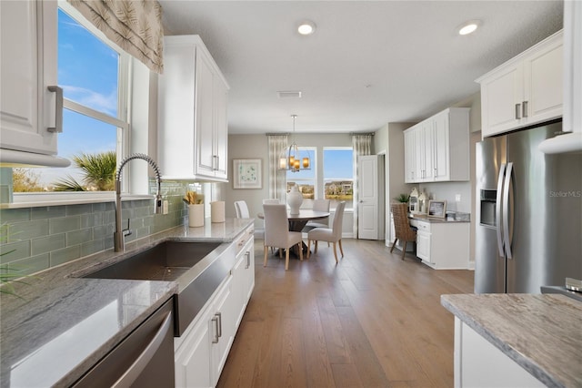 kitchen with stainless steel appliances, a healthy amount of sunlight, white cabinets, and light stone countertops