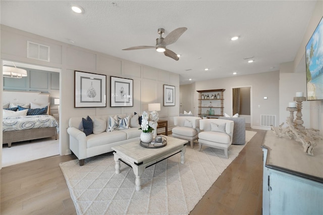 living room with light wood-style flooring, a ceiling fan, visible vents, and recessed lighting