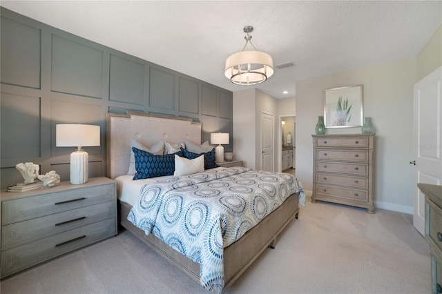 bedroom featuring a textured ceiling, connected bathroom, a decorative wall, light carpet, and visible vents