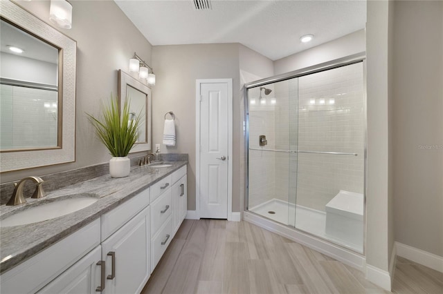 bathroom with double vanity, a shower stall, baseboards, and a sink