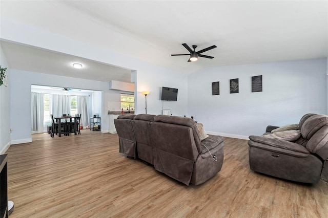 living room with a ceiling fan, baseboards, vaulted ceiling, and light wood finished floors