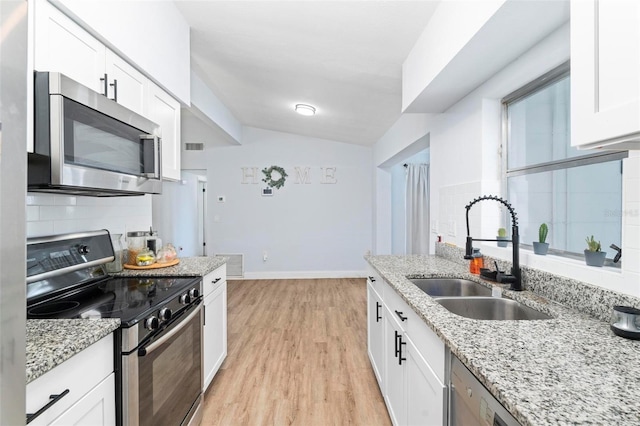 kitchen with light wood-style flooring, stainless steel appliances, a sink, white cabinets, and backsplash