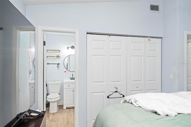 bedroom featuring a closet, visible vents, ensuite bathroom, a sink, and light wood-type flooring