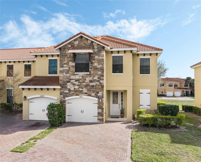 mediterranean / spanish-style house featuring stone siding, decorative driveway, a tile roof, and stucco siding