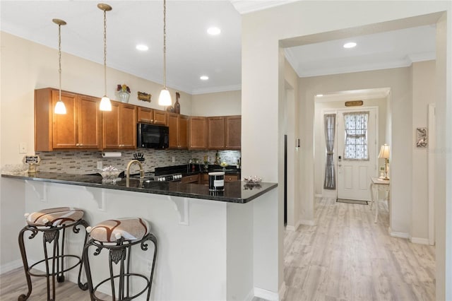 kitchen with brown cabinetry, ornamental molding, stove, a kitchen bar, and black microwave