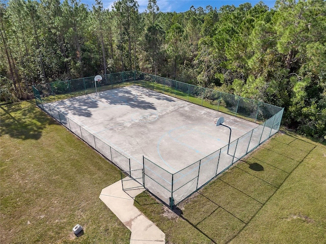 view of basketball court with community basketball court, a lawn, a wooded view, and fence