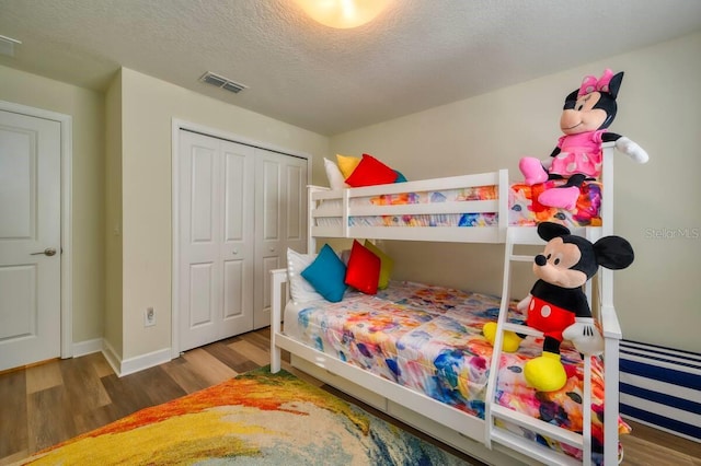 bedroom with a closet, visible vents, a textured ceiling, wood finished floors, and baseboards