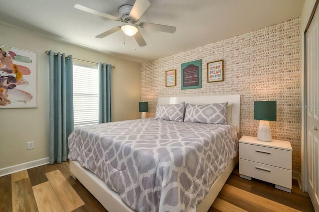 bedroom featuring an accent wall, a ceiling fan, baseboards, and wood finished floors