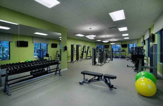 exercise room featuring a paneled ceiling and baseboards