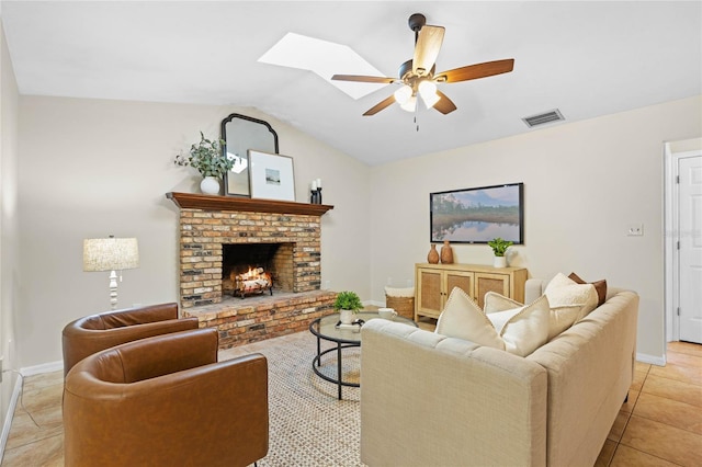 living area with light tile patterned floors, a ceiling fan, visible vents, vaulted ceiling with skylight, and a brick fireplace