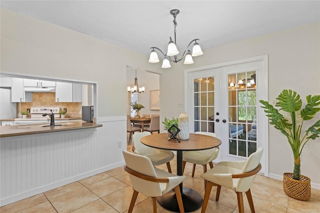 dining space with an inviting chandelier, light tile patterned floors, french doors, and wainscoting