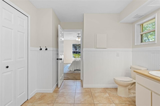 bathroom with tile patterned floors, wainscoting, toilet, and a healthy amount of sunlight