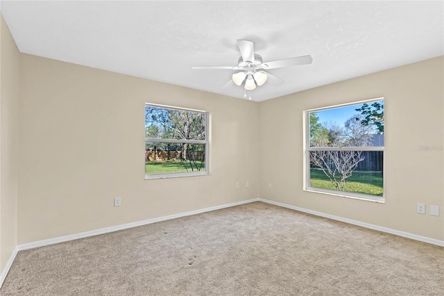 carpeted spare room with a healthy amount of sunlight, baseboards, and ceiling fan