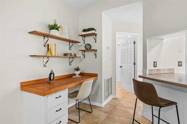 office with light tile patterned floors, visible vents, baseboards, and built in study area