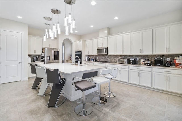 kitchen with light countertops, appliances with stainless steel finishes, a center island with sink, and white cabinets