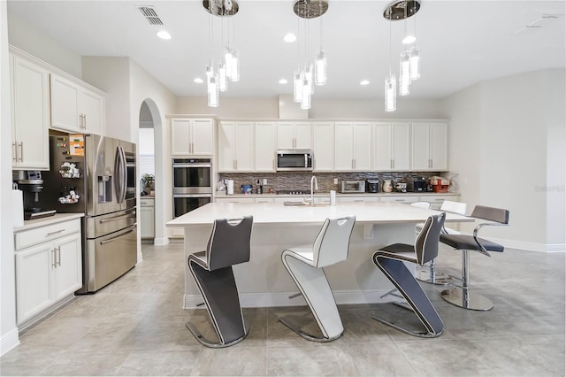 kitchen featuring stainless steel appliances, a sink, white cabinets, light countertops, and an island with sink