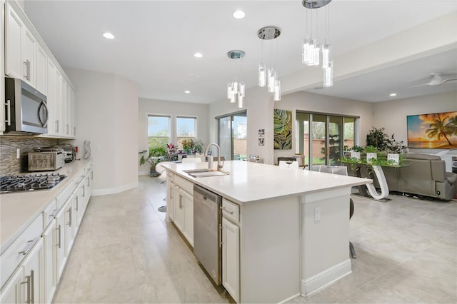 kitchen with stainless steel appliances, white cabinetry, open floor plan, light countertops, and a center island with sink