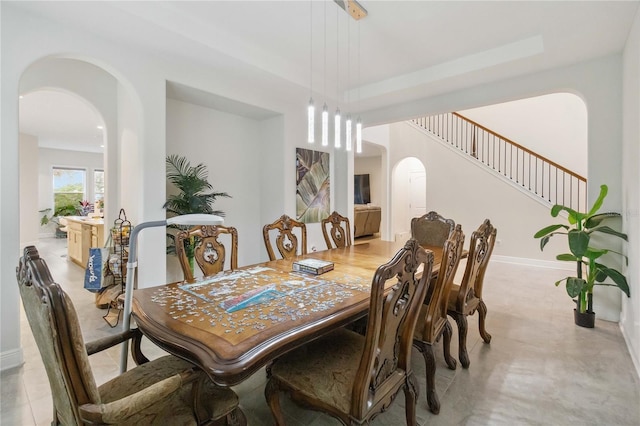 dining room featuring arched walkways, stairs, and baseboards