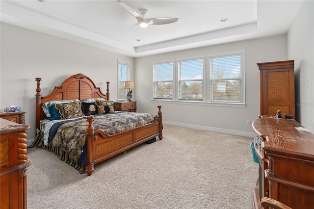 bedroom featuring light carpet, a raised ceiling, a ceiling fan, and baseboards