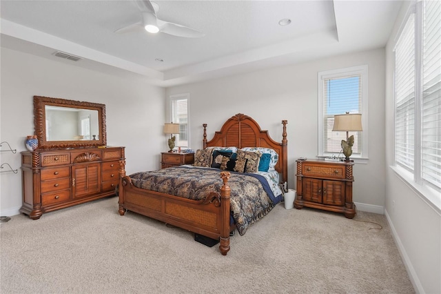 bedroom with light colored carpet, a raised ceiling, and visible vents