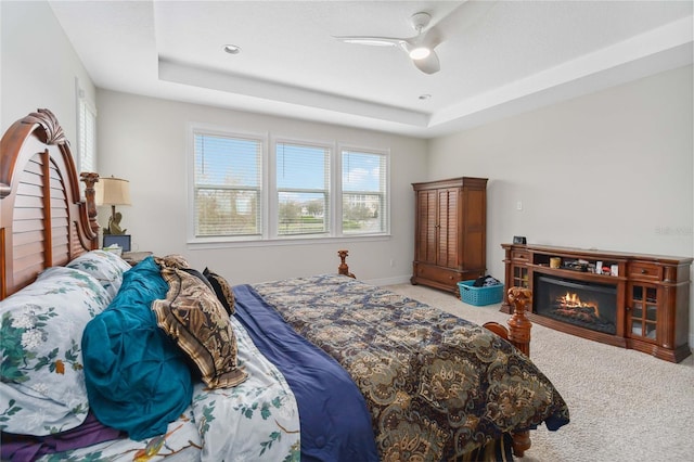 bedroom featuring ceiling fan, a lit fireplace, carpet flooring, and a raised ceiling