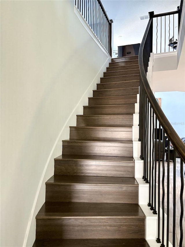 stairway with a towering ceiling, visible vents, and baseboards