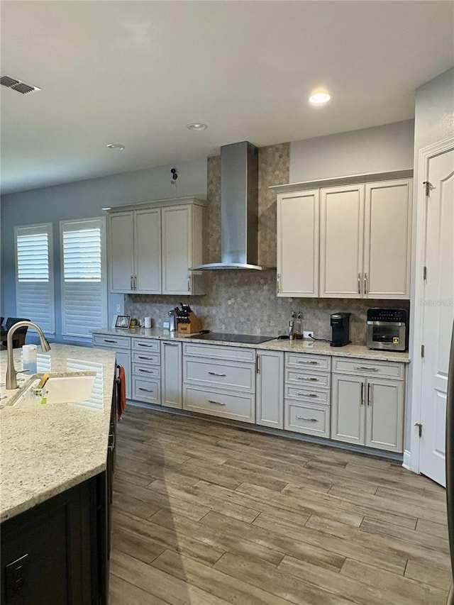 kitchen with black electric stovetop, tasteful backsplash, visible vents, a sink, and wall chimney exhaust hood