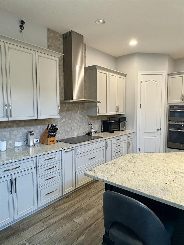 kitchen with light stone counters, dark wood-style flooring, backsplash, wall chimney exhaust hood, and black electric cooktop