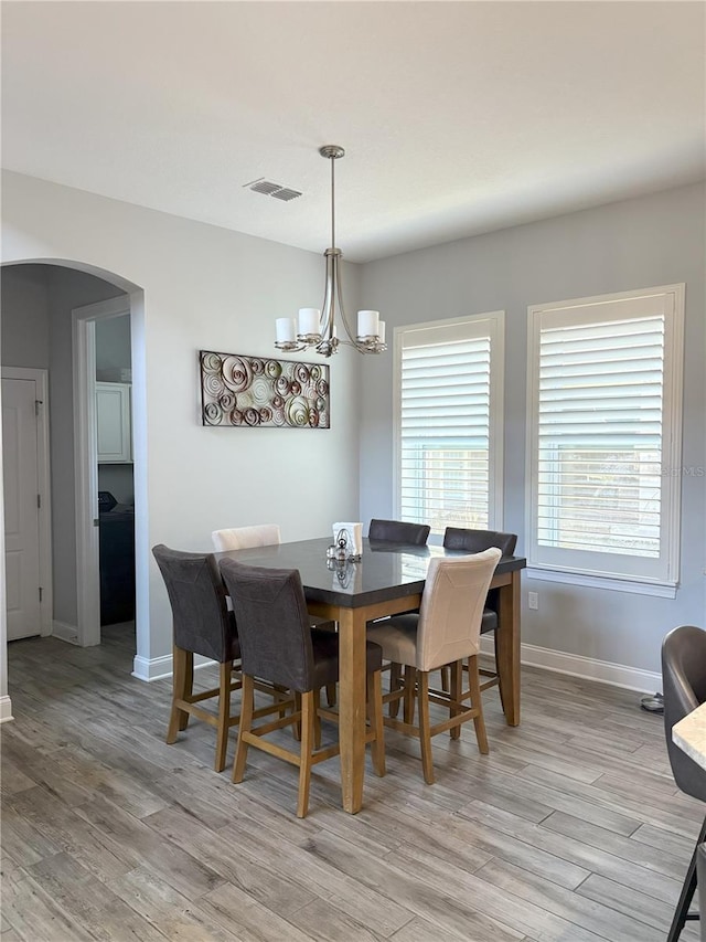 dining area with arched walkways, visible vents, a notable chandelier, and light wood finished floors