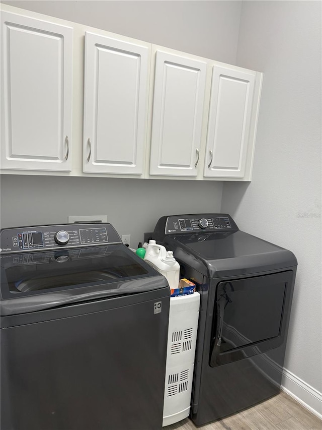 clothes washing area featuring cabinet space, baseboards, washer and clothes dryer, and wood finished floors