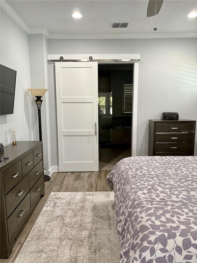 bedroom featuring recessed lighting, visible vents, a barn door, ornamental molding, and wood finished floors