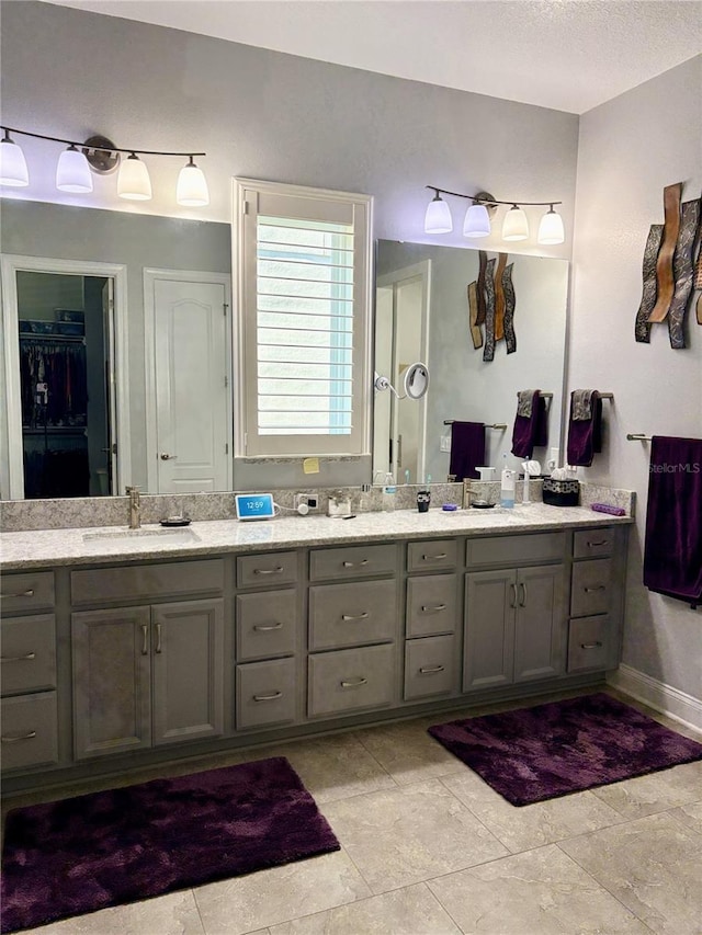 full bathroom with a textured ceiling, double vanity, a sink, and baseboards